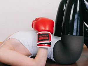 Close-up of Aido Akida, she lies on the floor, she is wearing a white swimsuit, red boxing gloves, black nylons and black latex stockings.