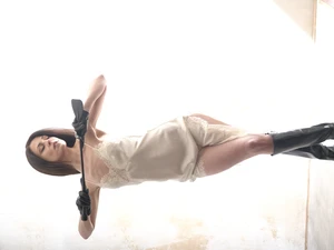 Aido Akida, Dominatrix, based in Berlin, she is wearing white silk lingerie, black leather boots, she is bathed in white light. She holds a black leather whip beneath her face, her eyes are shut. Strong pose