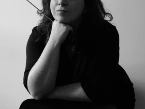 The Architect is leaning forward on a chair holding a cane and smiling