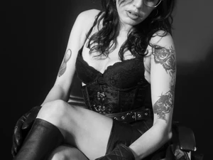 Madame Ava Laffaire in Lederrock, Korsett und Lederhandschuhe. Dabei zieht sie den Reißverschluss ihres Lederstiefel hoch.