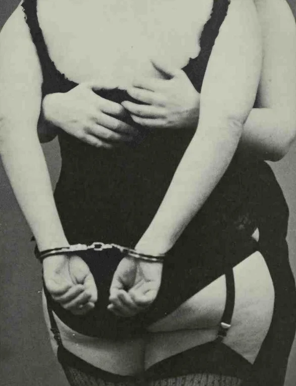 two women in black lingerie hugging while one wears handcuffs