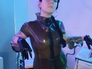 Lara Vixette trägt Latex und lehnt am Gyn Stuhl im Studio LUX