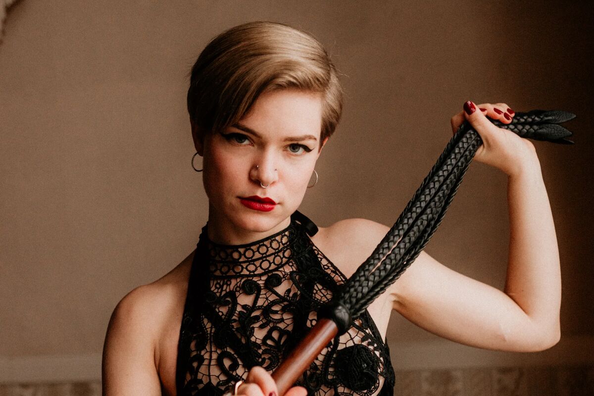 Leila Rose Wilde in einem Korsett während sie den Flogger schwingt im BDSM Studio LUX Berlin - herrische Domina