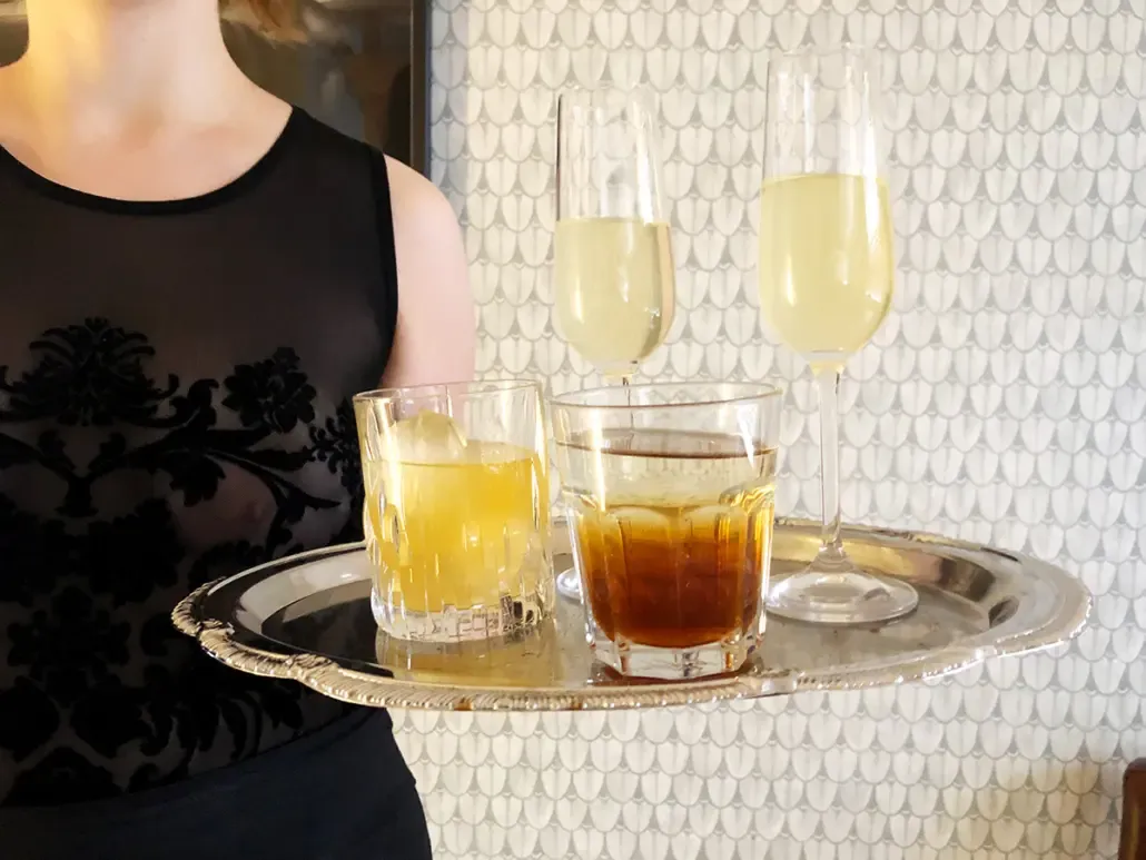 A silver tray of drinks is served by Lina Twist wearing a black lacey body at Studio LUX Berlin.
