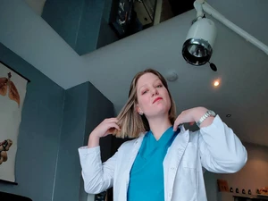 The bizarre Dr. Lina Twist, dressed in scrubs and a white coat, invites you for an examination on the gynecological chair at the Studio LUX Berlin clinic.