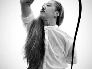 Ron mit langen Haaren und weißen Hemd hält eine Peitsche erhoben in der Hand, intensiver Blick nach oben, Schwarzweißporträt.