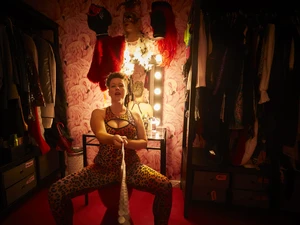 Tamara Solidor in hautengem Leo-Print mit tiefem Ausschnitt sitzt in der TV Ecke des Studio Lux und hält dich an einem Halsband fest