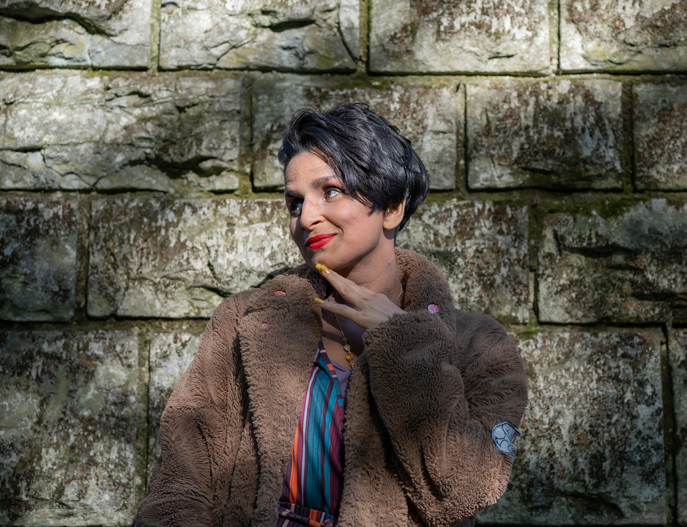 Violet Beau smiling and looking shocked in sunglasses in front of a stone wall